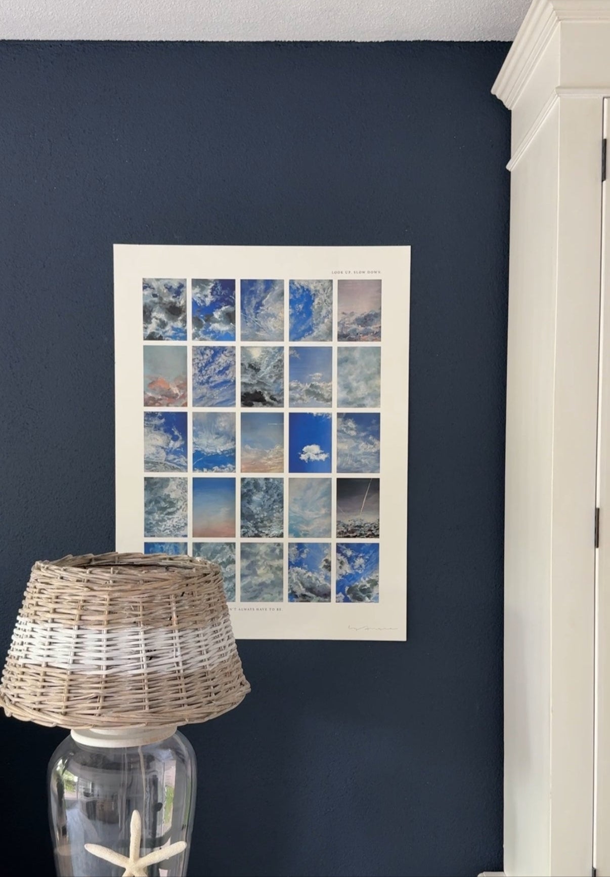 Nautical-themed decor with a lamp and starfish on a navy wall with a framed collage of blue sky and cloud images.